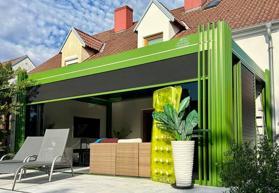 Ein moderner, grüner Innenhof mit einer ausfahrbaren Markise, Loungesesseln, einem Rattansitzbereich und tropischen Pflanzen.