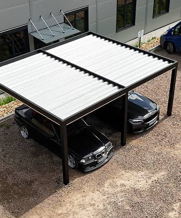Zwei schwarze Autos stehen unter einem modernen, freistehenden Carport mit Lamellendach aus Metall.