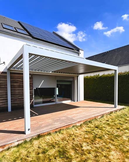Eine moderne Terrassenüberdachung mit Lattenrost, mit Blick auf eine Holzterrasse und eine Rasenfläche, unter strahlend blauem Himmel.